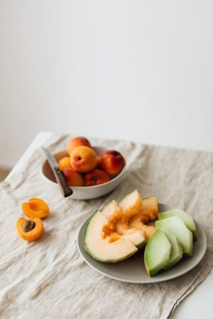 plate of fresh assorted melons served on table with bowl of ripe apricots