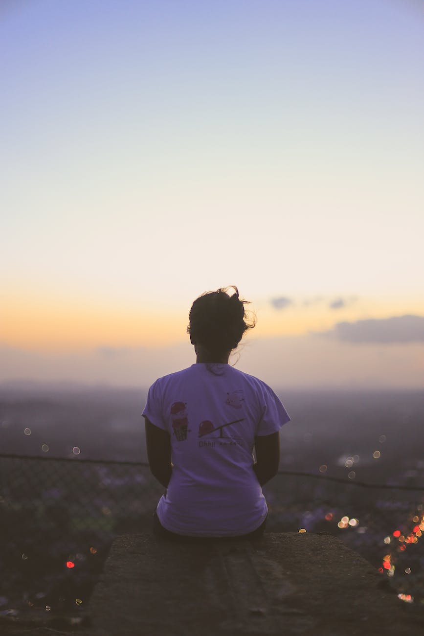 person in white shirt sitting on top of building during sunset